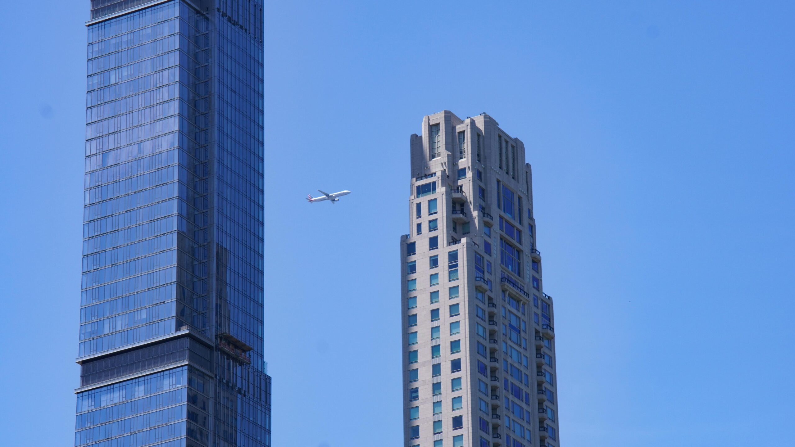 24/7 LGA Shuttle Service: Your Ultimate 2025 Guide to Conquering NYC’s Airport Chaos 1 An airplane flying between two towering skyscrapers in Manhattan, New York City.