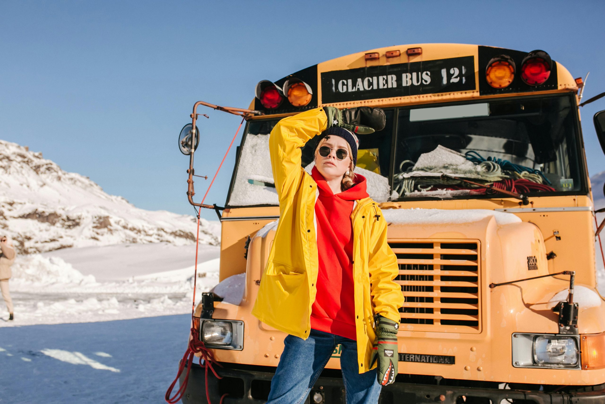 School Trip Bus Rental NYC: 6 Honest Comparisons Every First-Timer Needs in 2026 1 Fashionable woman in yellow coat poses beside glacier bus in snowy winter landscape.