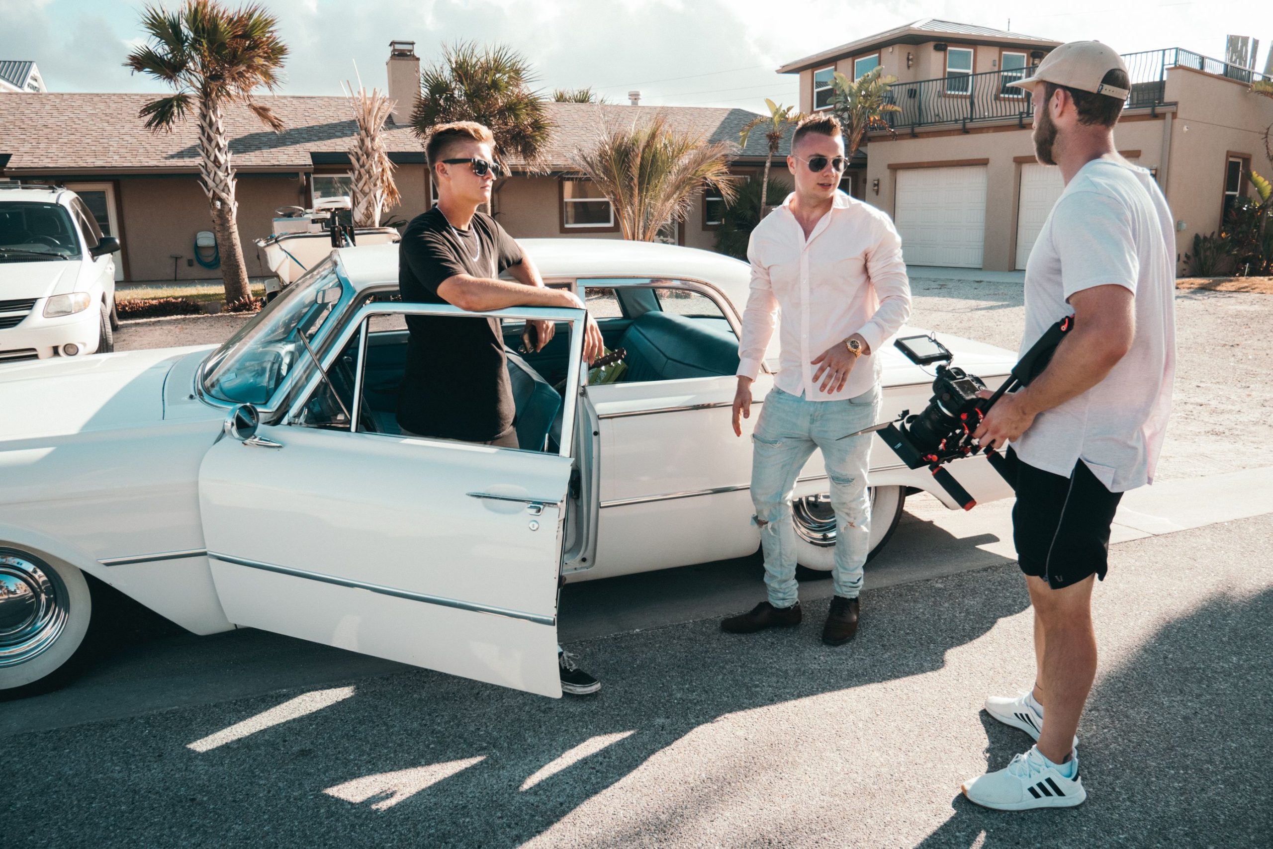 Production Crew Transportation in NYC: 7 Smart Ways to Move Your Crew Effortlessly in 2026 4 Three men with camera equipment near a classic car on a sunny day, showcasing filming outdoors.