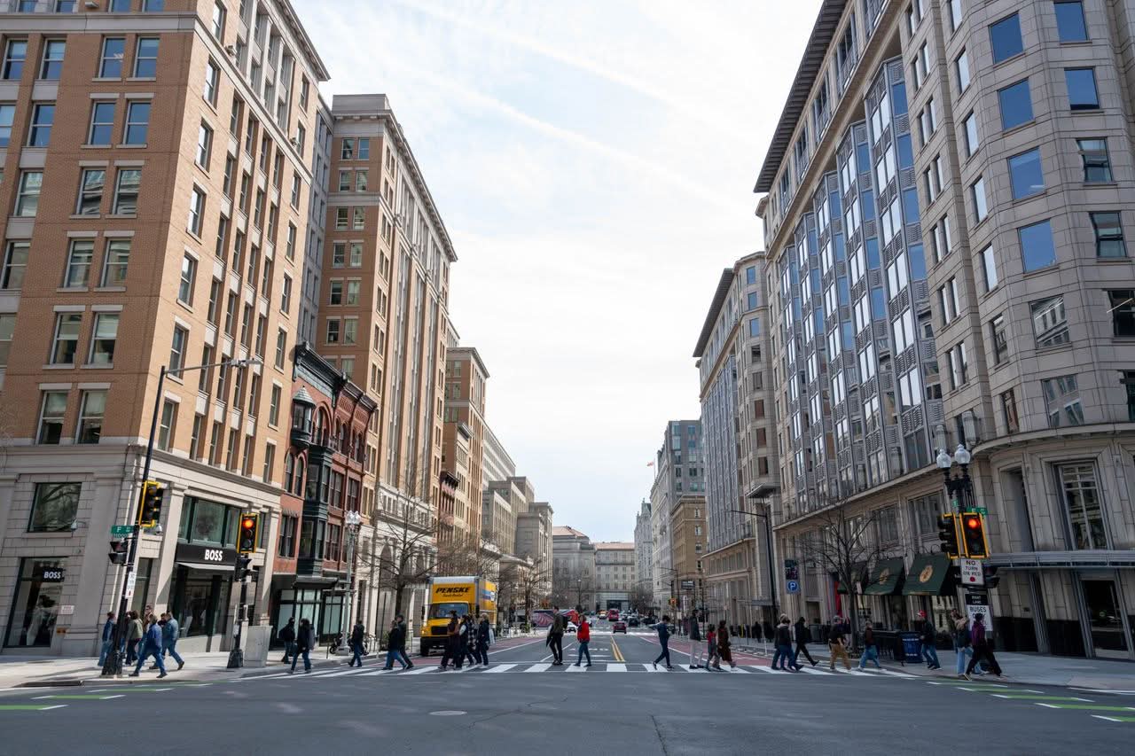 Downtown Washington DC road with high-rise buildings and pedestrians crossing.