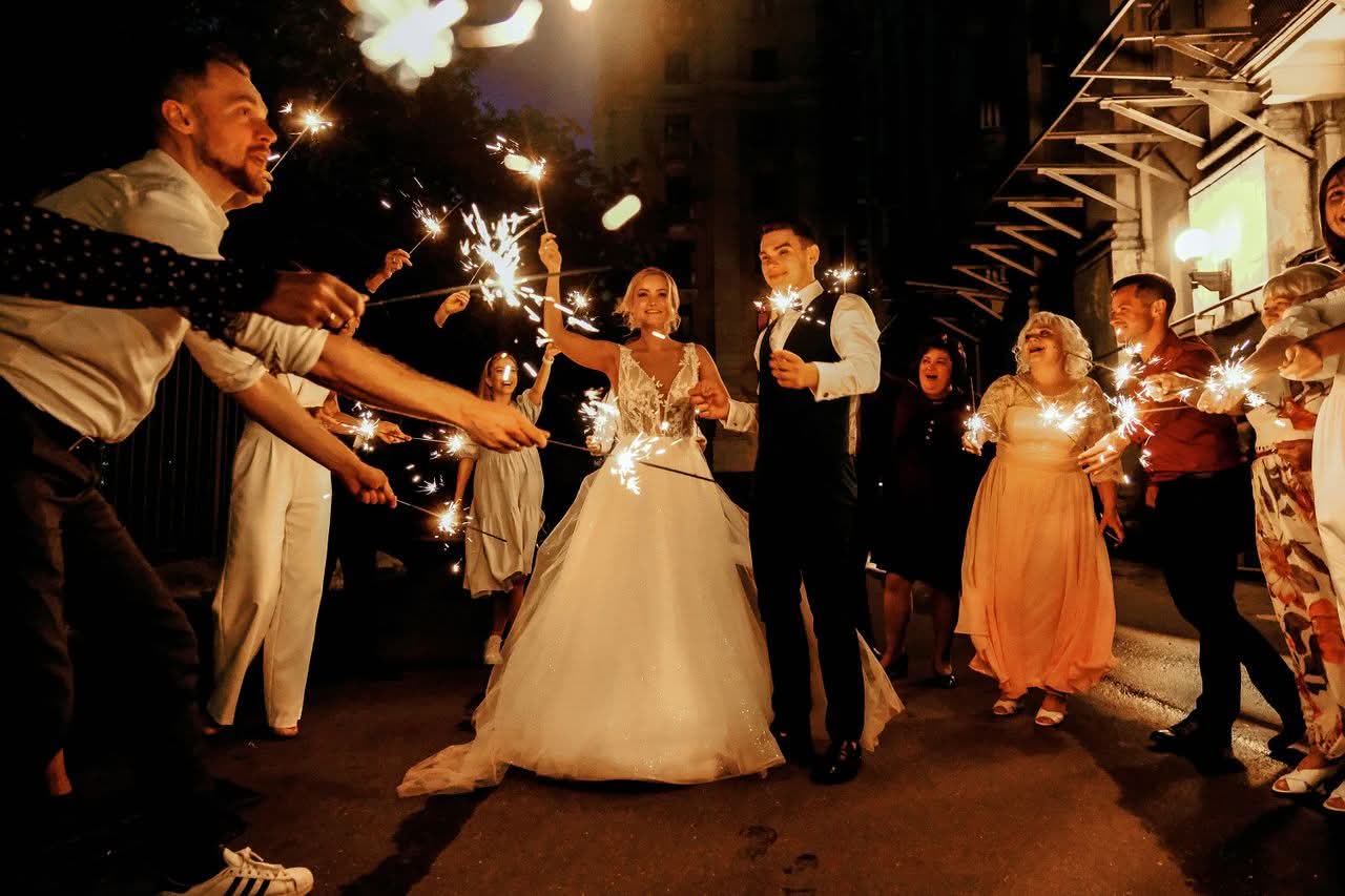 Wedding Transportation NYC for Groups: The Honest 2026 Guide 1 Full body of joyful young bride and groom with sparklers in hands walking near happy guests during wedding celebration in evening